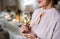 A midsection of a senior woman standing indoors in a room set for a party, holding wine.