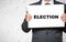 Midsection of smiling businessman holding election placard while standing against white brick wall