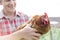 Midsection of smiling farmer holding hen at farm