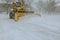 In midst of heavy snowstorm, snowplow truck removes snow from a car parking lot