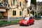 Milan, Italy - 29 july 2020: A red Fiat 500 car parked outside a house with sycamore trees, or chinar in the garden, in