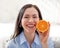 Miling woman in blue shirt holding orange in kitchen