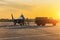 Military fighter is being pushed to a parking lot by a military vehicle at an air base in the evening at sunset