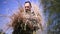 A military man is camouflaged outside by putting on a camouflage net with dry grass sticking out of it