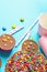 Milk Chocolate Birthday Cake with Multicolored Glazed Candy Sprinkles Buttercups Paper Drinking Cups Pink Straws Blue Background