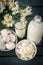 Milk, a plate of cottage cheese, white chicken eggs, a bouquet of flowers , daisies on a gray wooden background, dairy protein