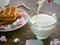Milk is poured into a cup from a bottle. Part of the milk spilled ha table. On a saucer are cookies and sweets.