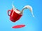 Milk splash in red mug and saucer jumping on blue background