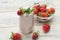 A milkshake made from fresh strawberries stands on a light wooden background