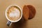 Milky frothy coffee in white mug next to a couple of round waffle biscuits isolated on light wood from above.