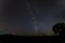 The Milky way over a black silhouette horizon with a tree