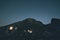 The Milky Way over the mountains, long exposure on the italian-french Alps, mountain hut and refuge illuminated. Toned image, vint