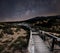 Milky way starscape above wood board walk pathway leading across sand dunes with grass