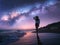 Milky Way and young woman in hat on the beach against starry sky