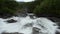 Milky white massive long waterfall down slippery valley rocks and stones in summer