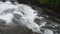 Milky white massive long waterfall down slippery valley rocks and stones in summer