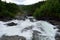 Milky white massive long waterfall down slippery valley rocks and stones in summer