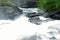 Milky white massive long waterfall down slippery valley rocks and stones in summer