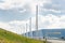 Millau Bridge piers disappear between distant hills across valley and green grassy slope, France.