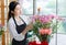 Millennial Asian young female flower shopkeeper decorator florist employee worker in apron standing smiling taking care by using