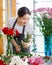 Millennial Asian young female flower shopkeeper decorator florist employee worker in apron standing smiling at workshop table