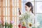 Millennial Asian young professional female flower shopkeeper owner decorator smiling using smartphone taking photo of decorating