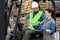 Millennial bearded man in helmet in forklift truck, discussing order with smiling woman