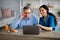 Millennial caregiver showing elderly disabled man in wheelchair how to use laptop at retirement home