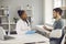 Millennial caucasian man patient with broken hand talk to afro american doctor