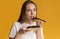 Millennial Girl Enjoying Chocolate Eclairs, Eating Unhealthy Sweets Over Yellow Background