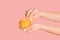 Millennial girl peeling fresh orange fruit on pink background, close up of hands