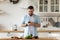 Millennial guy standing on domestic kitchen holds smartphone searching recipes