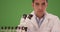 Millennial Hispanic medical research scientist using microscope on green screen