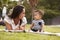 Millennial Hispanic mother lying beside her baby, sitting on a blanket in the park, close up