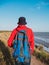 Millennial man in bucket hat red hoody backpack autumn sea background back view. Authentic male tourist lifestyle photo