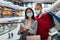 Millennial multiracial couple in face masks checking shopping list in mobile app, holding shopper bags at mall