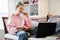 Millennial teen girl sit at couch in living room study on laptop making notes