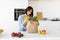 Millennial woman unpacking paper bag with fresh organic vegetables and fruits, standing in modern kitchen
