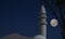 Minaret of a mosque in Jordan with dark blue evening sky and a full moon in the background. Elements of this image furnished by