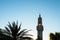 Minaret of mosque and silhouette of date palm on blue sky background in sunny day, copy space