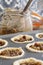 Mince pies in a baking tray with mincemeat in a clip glass jar and a spoon.  On a wood worktop