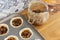 Mince pies in a baking tray with mincemeat in a clip glass jar and a spoon.  On a wood worktop