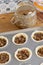 Mince pies in a baking tray with mincemeat in a clip glass jar and a spoon.  On a wood worktop