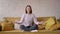 Mindful calm beautiful mixed race woman sit at sofa doing yoga breath exercise at home take break relax eyes closed