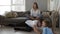 Mindful caucasian mother meditating sitting on sofa while active energetic child daughter jumping playing around and