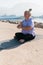 Mindful senior woman with dreadlocks meditating by the sea and beach - wellness and yoga practice
