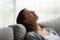 Mindful young woman daydreaming alone indoors on couch.