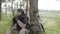 Mine clearance. Soldier with mine detector and backpack sits exhausted by a tree after heavy demining