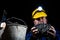 A miner stands holding a large lump of coal in his hands and wearing a helmet with a glowing flashlight