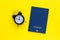 Mini alarm clock and passport on yellow background. Time to travel or vacation. World Tourism Day. Flat lay, top view with copy